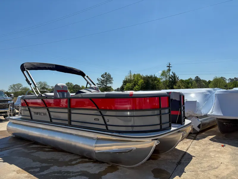 Slide: The Image of 2025 Trifecta 22RF CS pontoon boat with red and gray design, parked outdoors. - 3