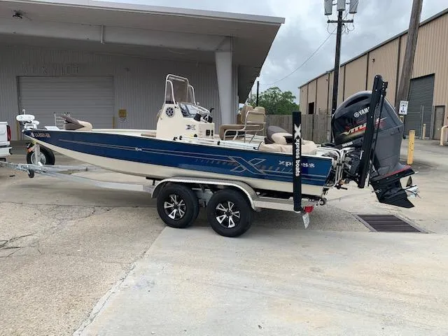 Slide: The Image of 2024 Xpress H22 boat on trailer, blue and white design, parked outside industrial building. - 2