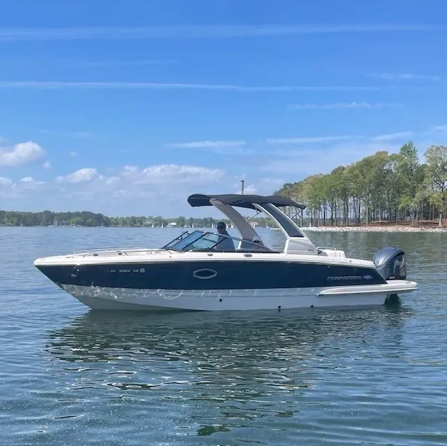 The Image of 2022 Chaparral 267 SSX OB boat on a calm lake under a clear blue sky. - 1