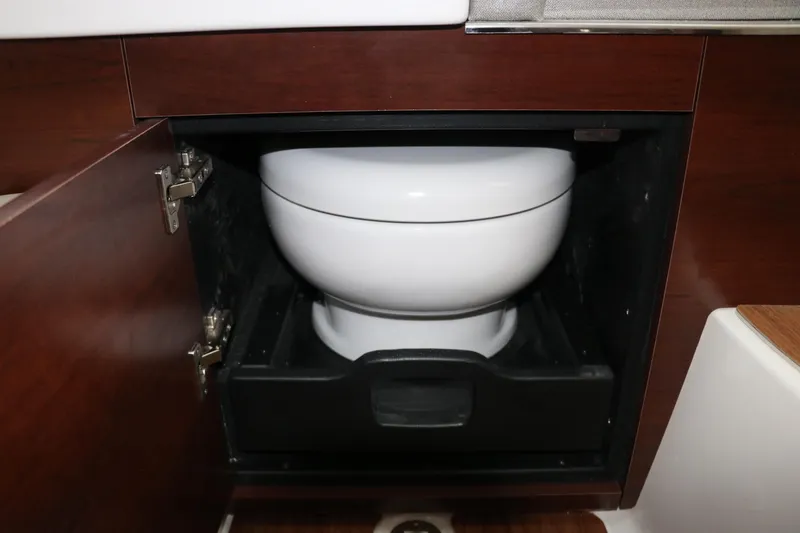 Slide: The Image of 2025 Chaparral 280 OSX boat interior with a compact toilet in a wooden cabinet. - 36