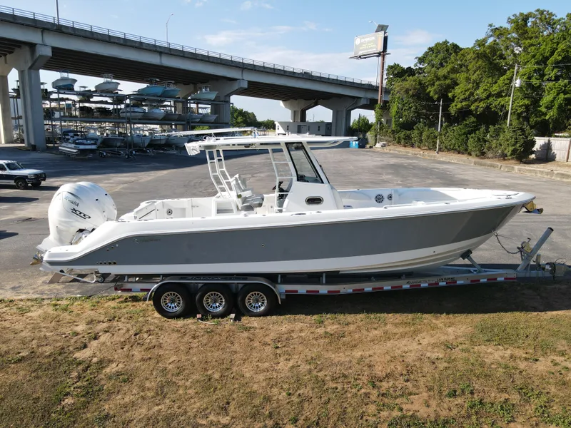 Slide: The Image of 2024 Edgewater 340CC boat on trailer, parked near a bridge and trees. - 34