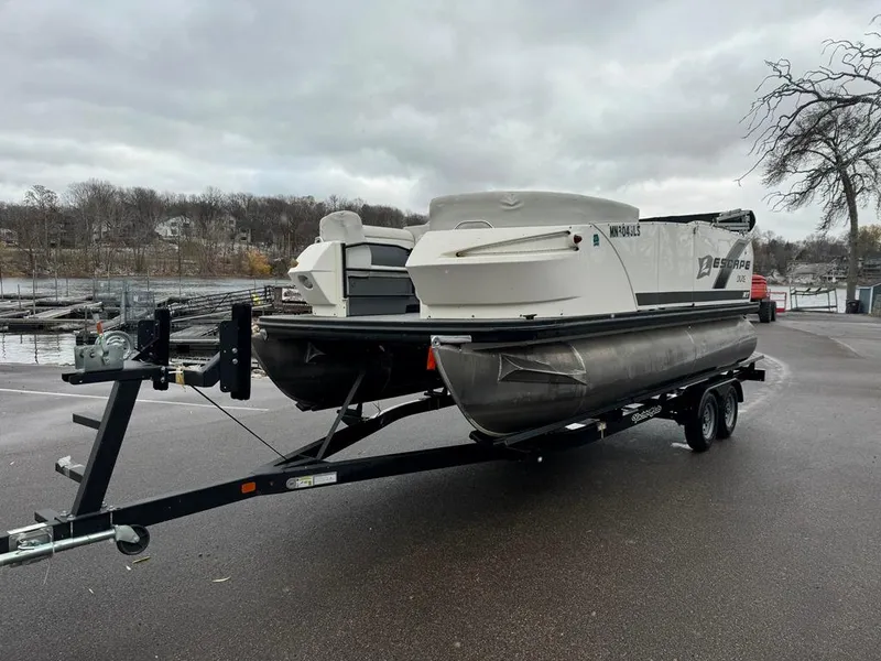 Slide: The Image of 2017 Larson Escape Cruze pontoon boat on trailer, parked near a lake on a cloudy day. - 4