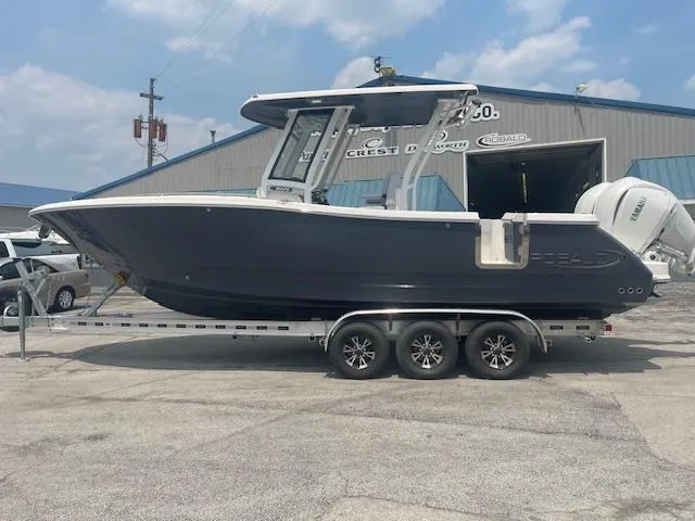 Slide: The Image of 2025 Robalo R270 Center Console boat on trailer, parked outside a warehouse. - 0