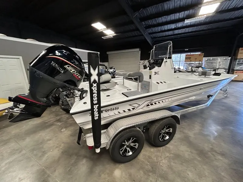 Slide: The Image of 2025 Xpress H 210 Bay boat on trailer in showroom, featuring powerful outboard motor. - 2