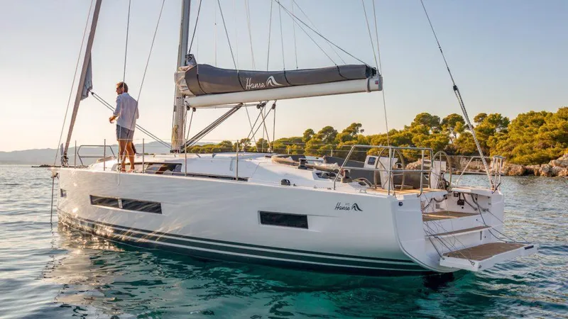 Slide: The Image of 2025 Hanse 410 yacht sailing on calm waters near a forested shoreline. - 16