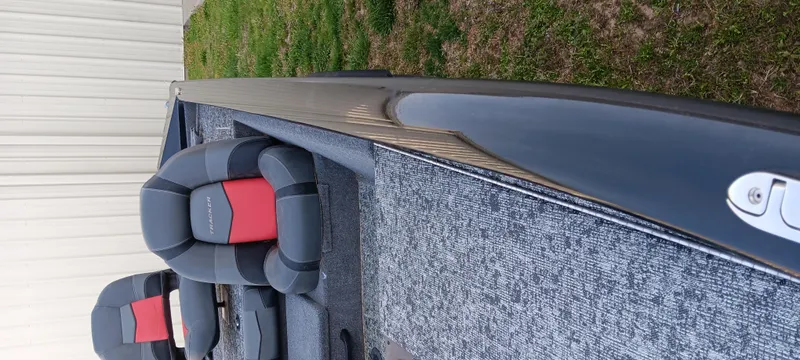 Slide: The Image of 2025 Tracker Pro Team 190 boat interior with gray and red seating on grass. - 9