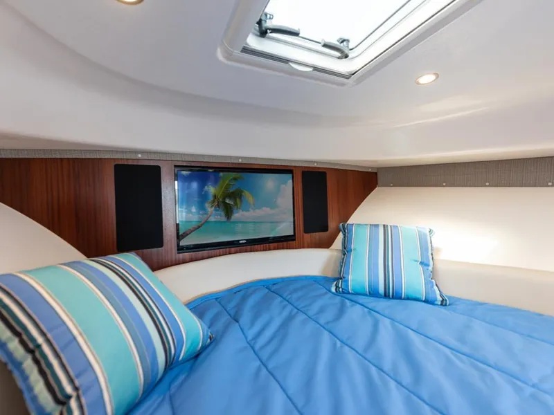 Slide: The Image of 2018 Pursuit OS 385 Offshore cabin with blue bedding, striped pillows, and a TV. - 30