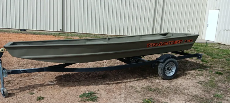 Slide: The Image of 2025 Tracker Grizzly 1436 Utility boat on trailer, parked outdoors near a metal building. - 2