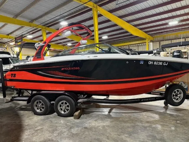 Slide: The Image of 2016 Four Winns TS242 boat in a showroom, red and black design on a trailer. - 1