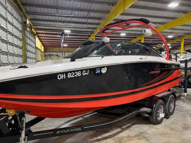 Slide: The Image of 2016 Four Winns TS242 boat in storage, black and red design, on a trailer. - 2