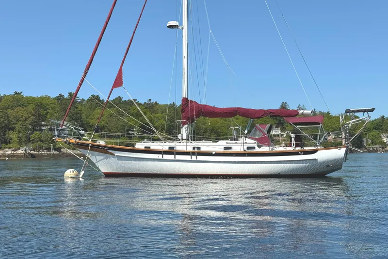 The Image of 1988 Cabo Rico 38XL sailboat anchored on calm water with lush green shoreline. - 0