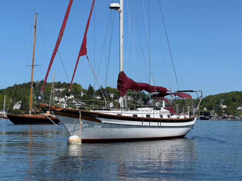 Slide: The Image of 1988 Cabo Rico 38XL sailboat anchored in calm waters, featuring maroon sails and scenic background. - 2