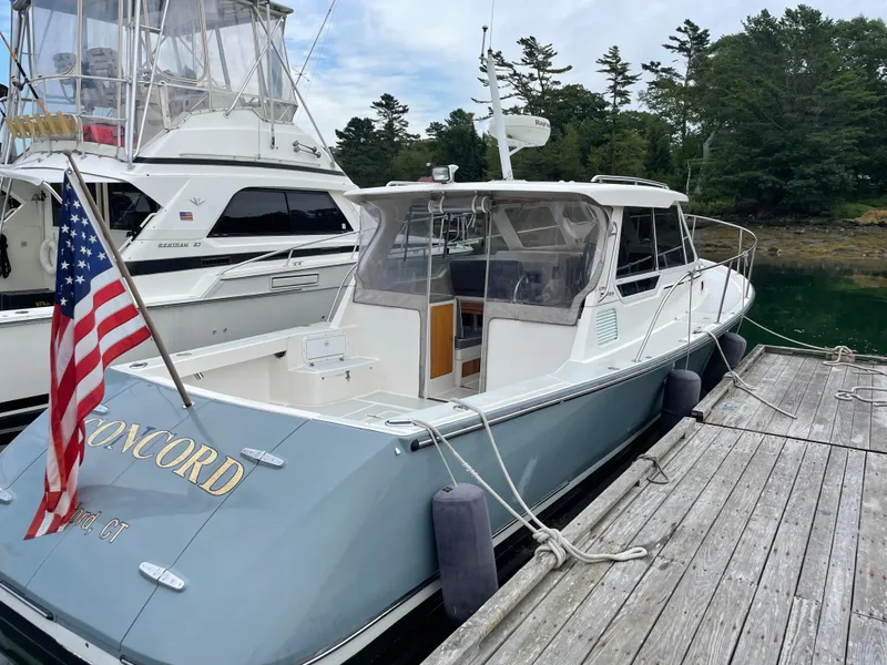 Slide: The Image of 2005 True North 33 boat docked, American flag, calm water, trees in background. - 2