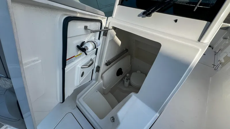 Slide: The Image of 2022 Pursuit S 268 boat interior with compact marine toilet and storage compartment. - 22