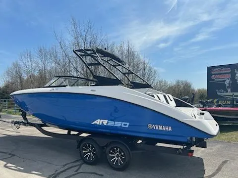 Slide: The Image of 2025 Yamaha AR250 boat in blue on a trailer, parked outdoors. - 2