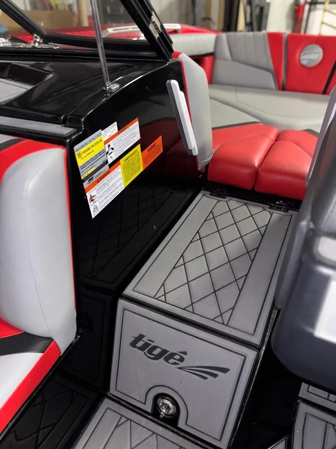Slide: The Image of 2018 Tigé RZX3 boat interior with red and gray seating, safety labels, and logo. - 23