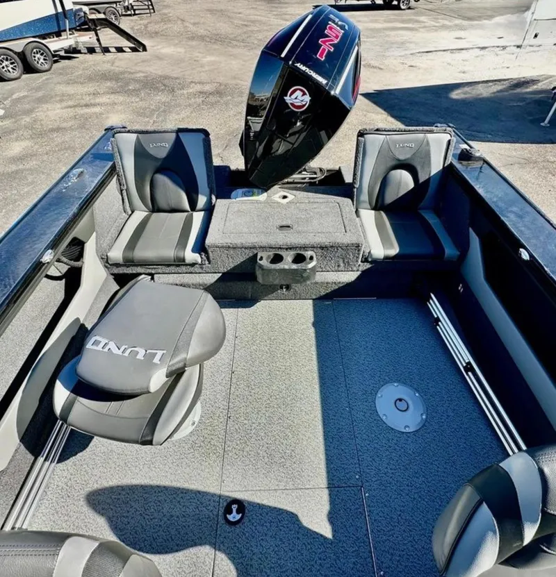 Slide: The Image of 2025 Lund 1875 Crossover XS boat interior with seating and motor, in a parking area. - 16