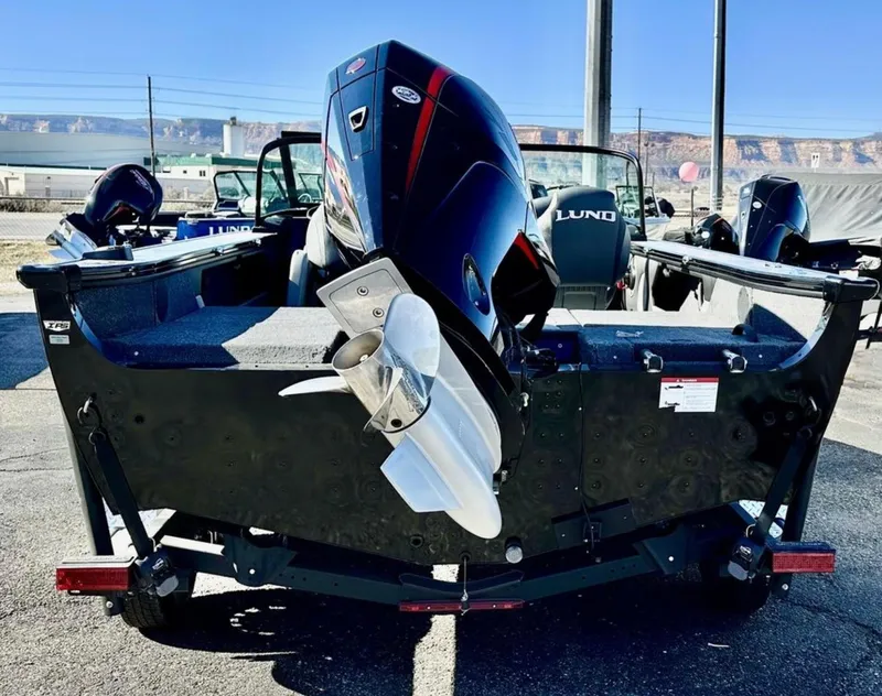 Slide: The Image of 2025 Lund 1875 Crossover XS boat, rear view with outboard motor, parked outdoors. - 3