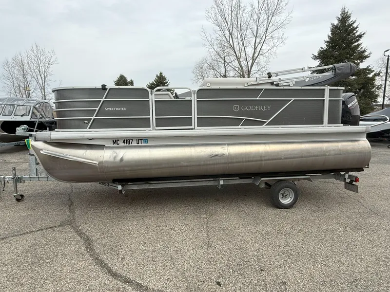 Slide: The Image of 2022 Godfrey Sweetwater 1886 FX pontoon boat on trailer, parked outdoors. - 2