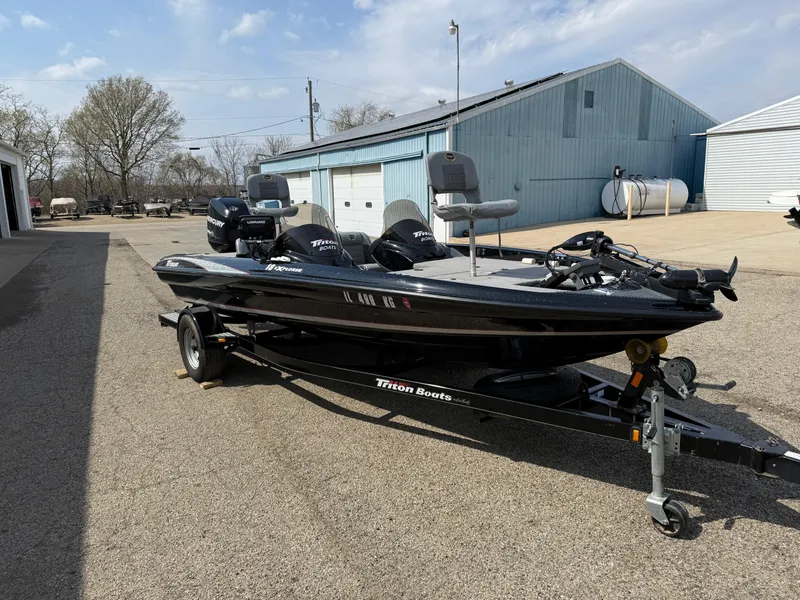 Slide: The Image of 2009 Triton 18 Explorer boat on trailer, parked outdoors near industrial buildings. - 3