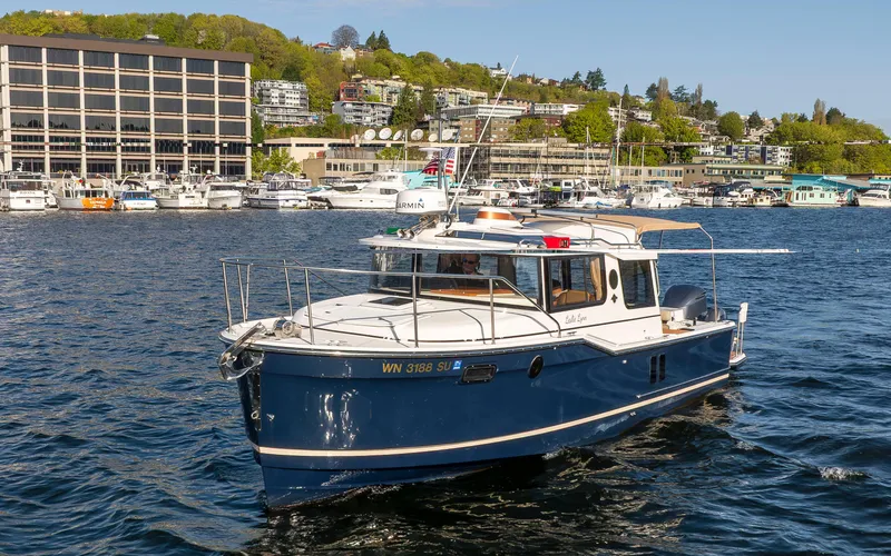 Slide: The Image of 2020 Ranger Tugs R-27 boat on a scenic waterfront with buildings and greenery. - 0