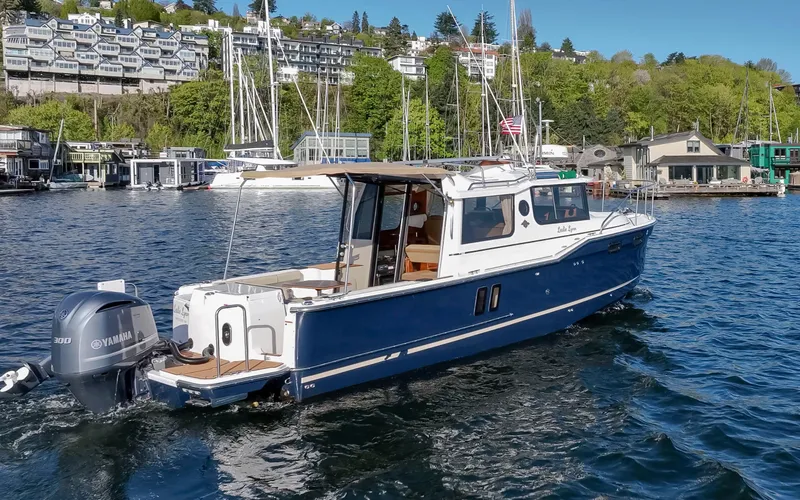 Slide: The Image of 2020 Ranger Tugs R-27 boat cruising on a scenic waterfront with sailboats and greenery. - 17