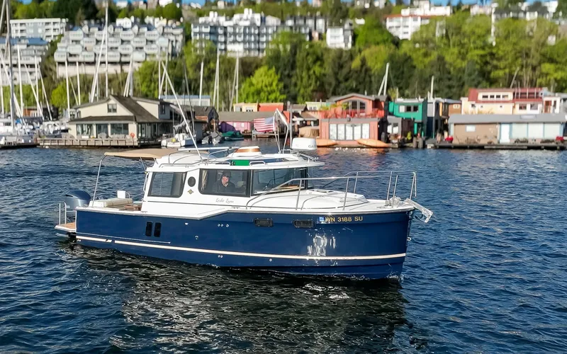 Slide: The Image of 2020 Ranger Tugs R-27 boat cruising on a scenic waterfront with buildings in the background. - 20