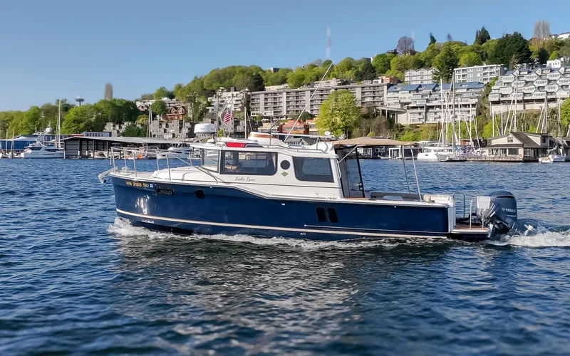 Slide: The Image of 2020 Ranger Tugs R-27 cruising on a scenic waterfront with buildings and greenery. - 22