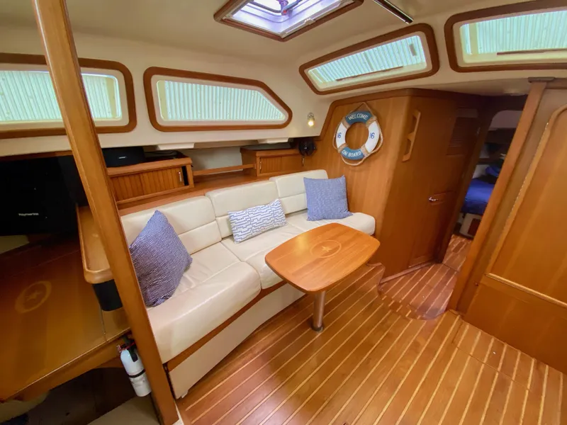 Slide: The Image of 2006 Island Packet 485 Center Cockpit interior with cozy seating and wooden accents. - 26
