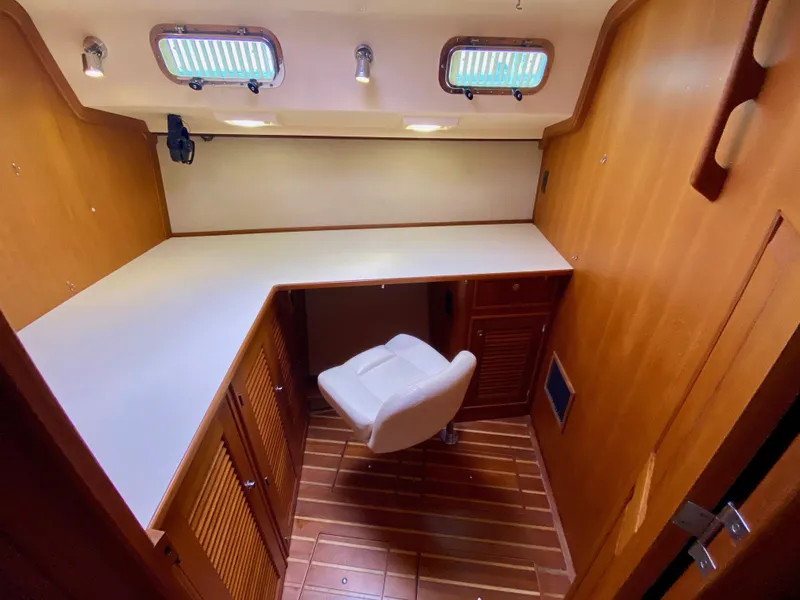 Slide: The Image of 2006 Island Packet 485 Center Cockpit interior with desk, chair, and wooden cabinetry. - 61