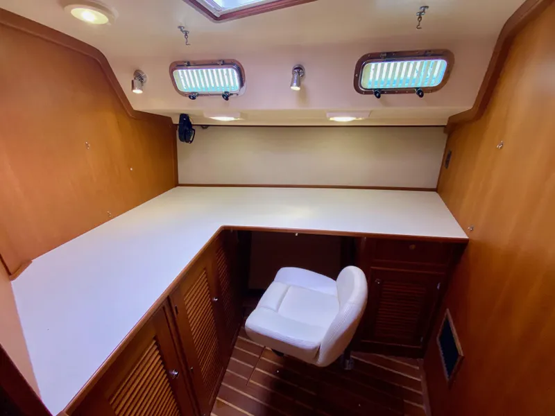 Slide: The Image of 2006 Island Packet 485 Center Cockpit interior with desk and chair, featuring wood cabinetry. - 62