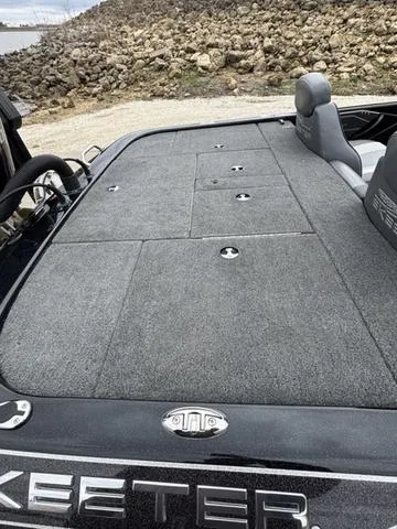 Slide: The Image of 2020 Skeeter ZX250 boat deck with storage compartments, gray carpet, and seating, near rocky shoreline. - 17