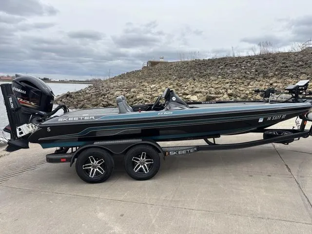 Slide: The Image of 2020 Skeeter ZX250 boat on trailer by rocky shoreline under cloudy sky. - 7