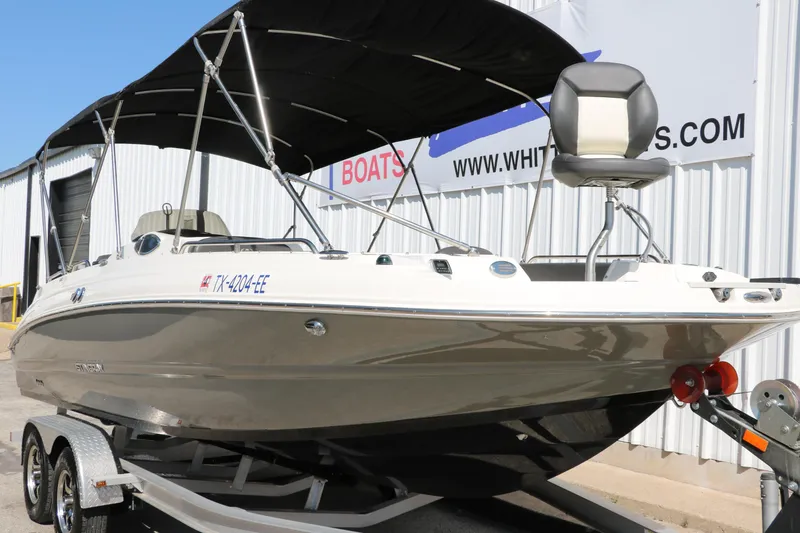 Slide: The Image of 2018 Stingray 212 SC boat on trailer with canopy, parked near a building. - 10