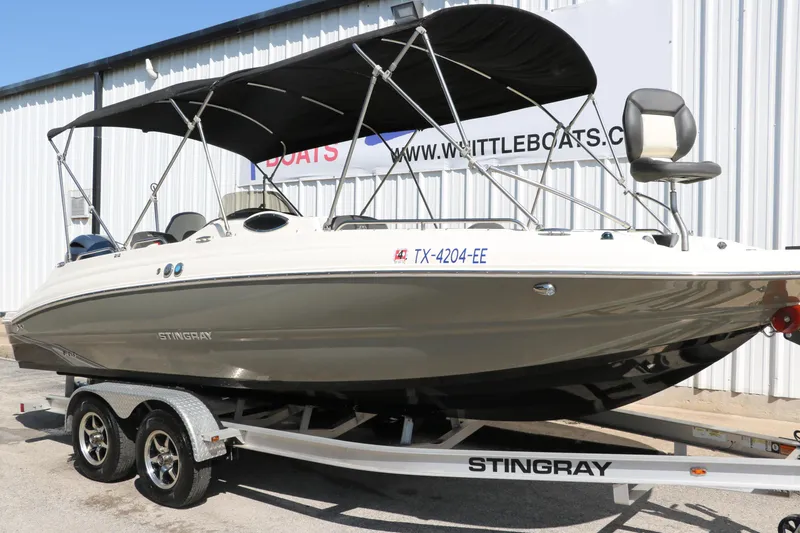 Slide: The Image of 2018 Stingray 212 SC boat on trailer with canopy, parked outside a building. - 11