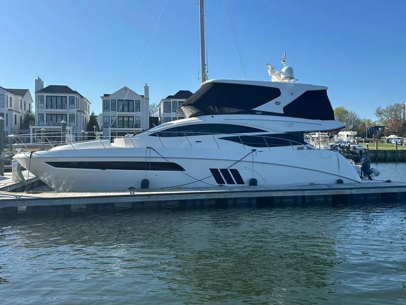 Slide: The Image of 2016 Sea Ray L590 Fly yacht docked at marina, with modern waterfront homes in background. - 2