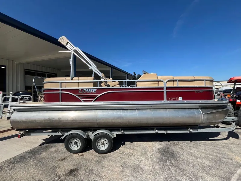 Slide: The Image of 2019 Lowe SS230W pontoon boat on trailer, parked outdoors under clear blue sky. - 4