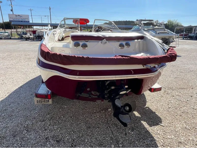 Slide: The Image of 2009 Tahoe Q71SSF boat rear view with maroon trim, parked on gravel. - 2