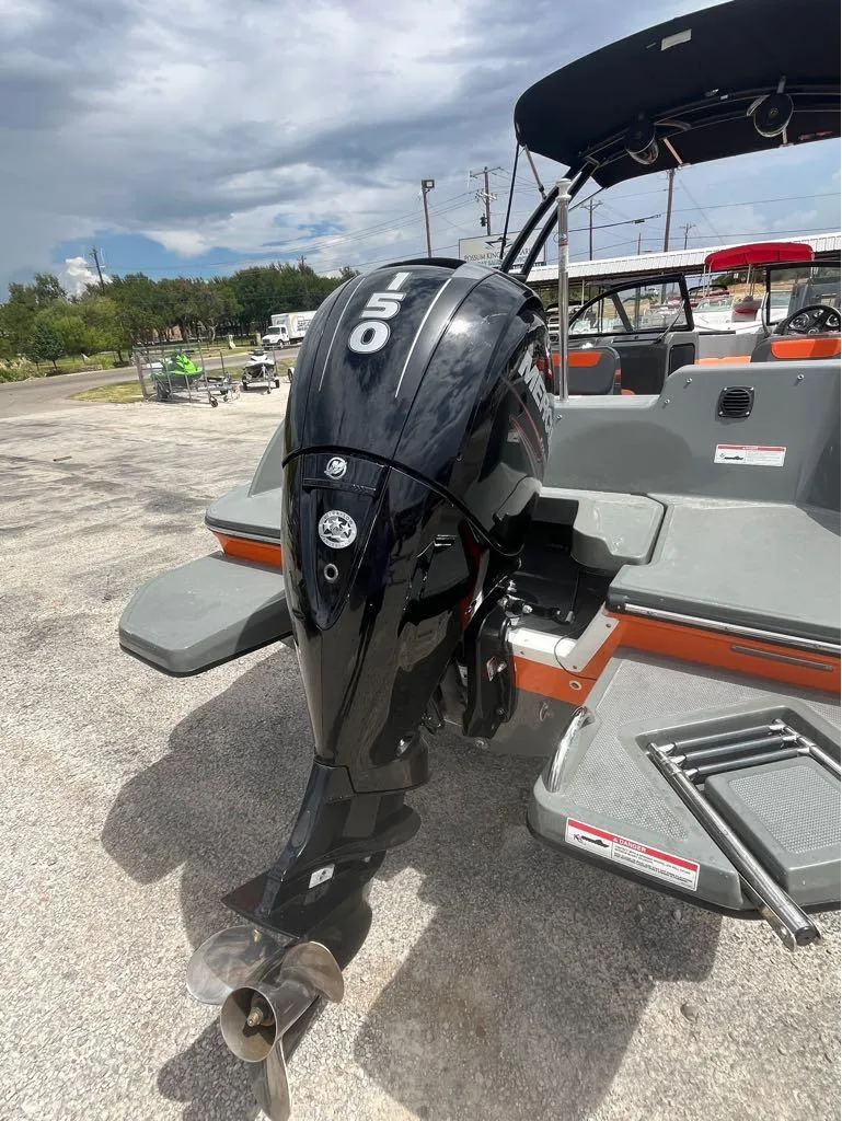 Slide: The Image of Bayliner 210 EL 2019 boat with a 150 HP outboard motor, parked outdoors. - 7
