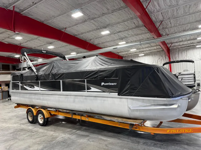 Slide: The Image of 2015 PlayCraft 2600 Sport Toon pontoon boat covered on trailer in indoor storage. - 18