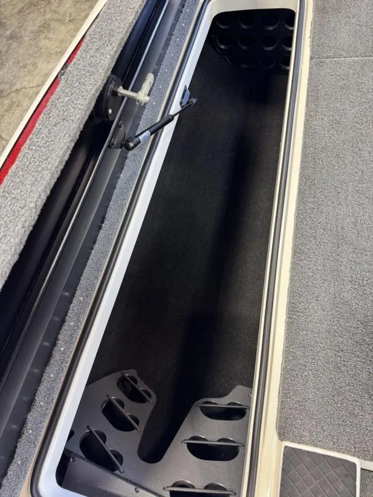 Slide: The Image of 2016 Triton 18 TrX boat storage compartment with rod holders and carpeted interior. - 38