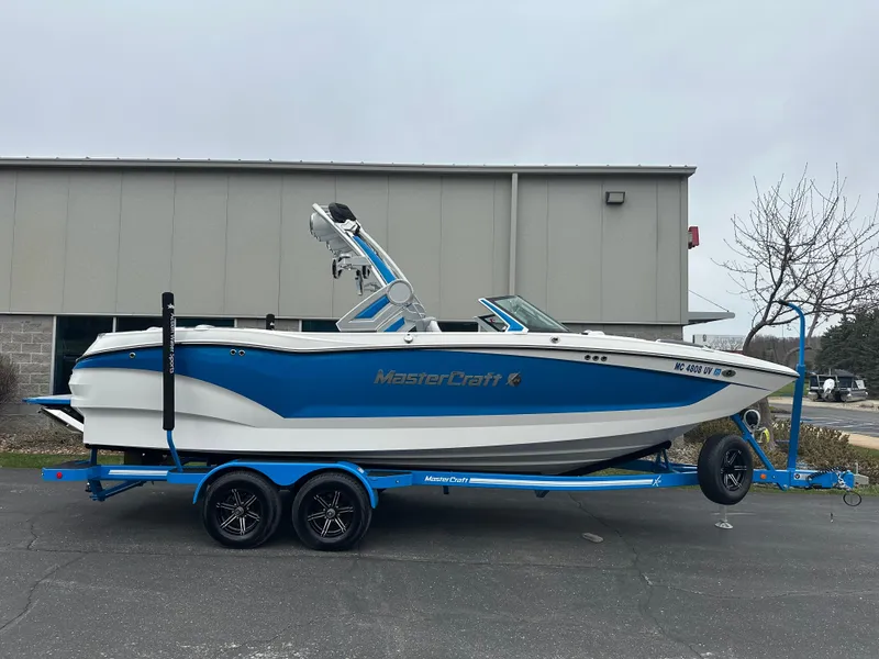 Slide: The Image of 2023 MasterCraft X24 boat on trailer, blue and white design, parked outside a building. - 1