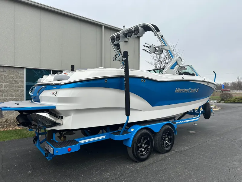 Slide: The Image of 2023 MasterCraft X24 boat on trailer, blue and white design, parked outside a building. - 4
