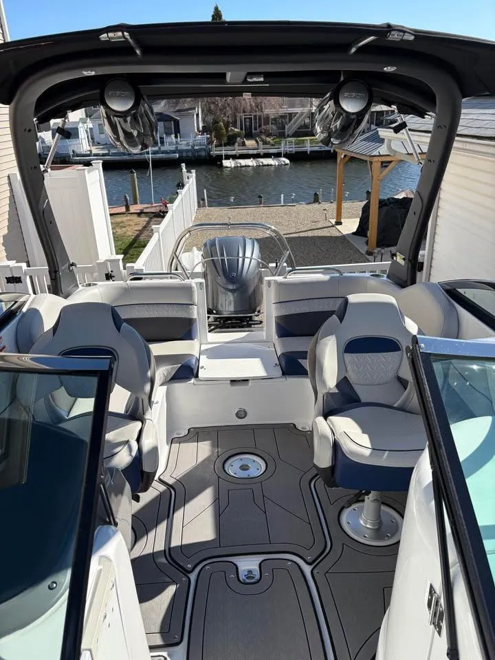 Slide: The Image of 2022 Hurricane SunDeck 2486 OB boat interior with seating and helm, docked by waterfront homes. - 2