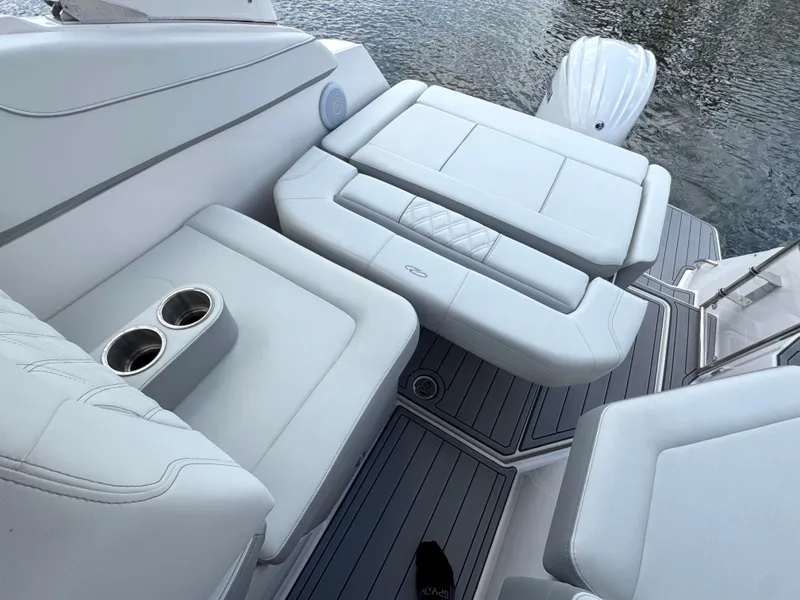 Slide: The Image of 2024 Regal 26 XO boat interior with white seating and cup holders, near water. - 13