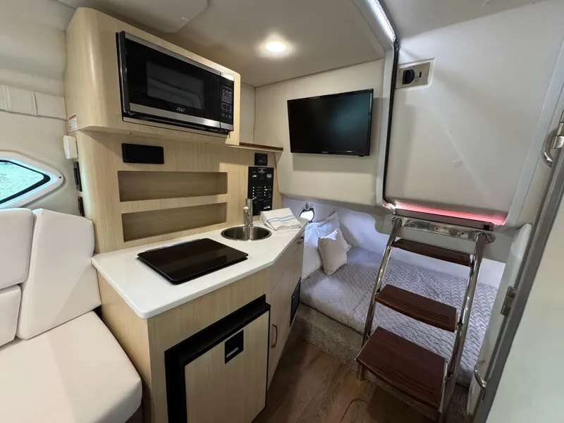 Slide: The Image of 2024 Regal 26 XO boat interior with kitchenette, microwave, TV, and cozy sleeping area. - 28