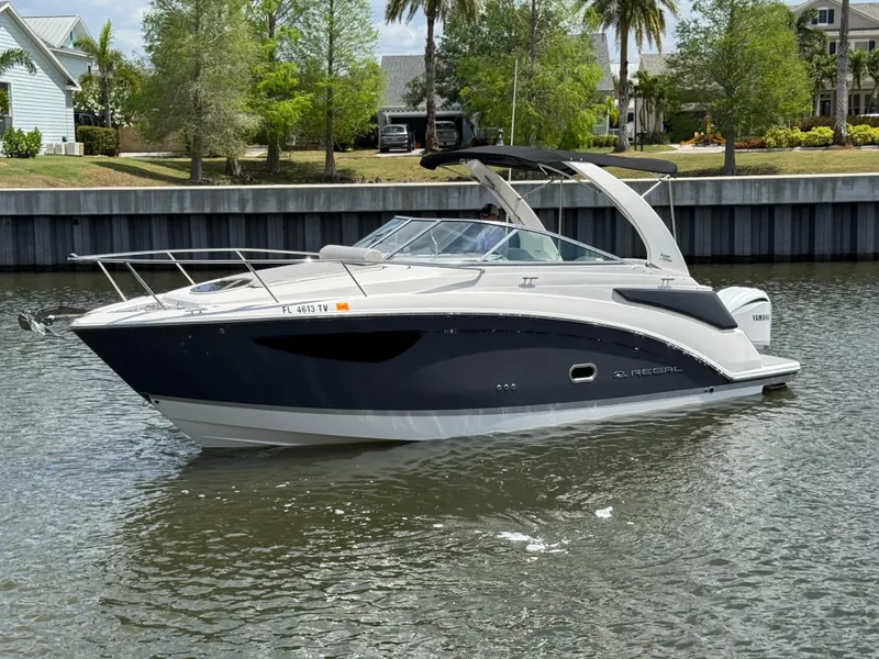 Slide: The Image of 2024 Regal 26 XO boat on a calm river, surrounded by lush greenery and waterfront homes. - 9