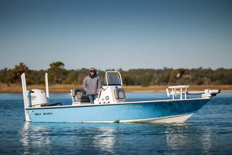 Slide: The Image of 2024 Sea Born FX22 Bay boat on calm water with a person at the helm. - 1