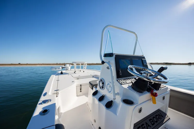 Slide: The Image of 2024 Sea Born FX22 Bay boat on calm water, showcasing steering console and clear blue sky. - 22