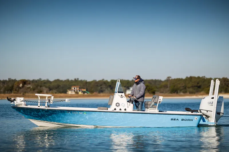 Slide: The Image of 2024 Sea Born FX22 Bay boat on calm water, with a person standing at the helm. - 8
